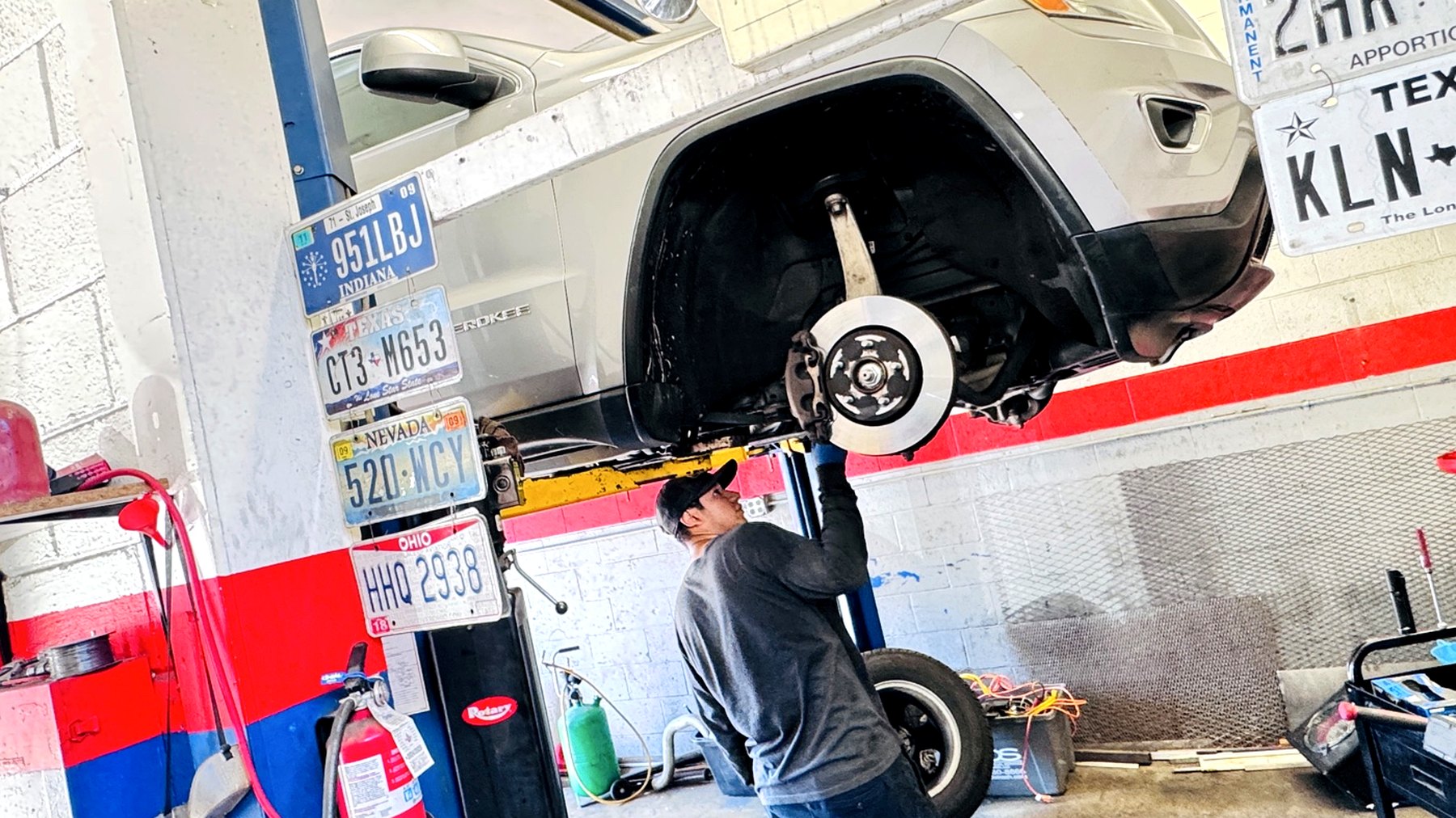 A Frontline Auto Plus technician inspecting a front brake rotor on a vehicle raised on the lift